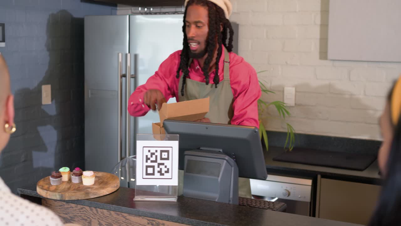 African American male barista arranging cupcakes on board after customer pointing serving via tongs