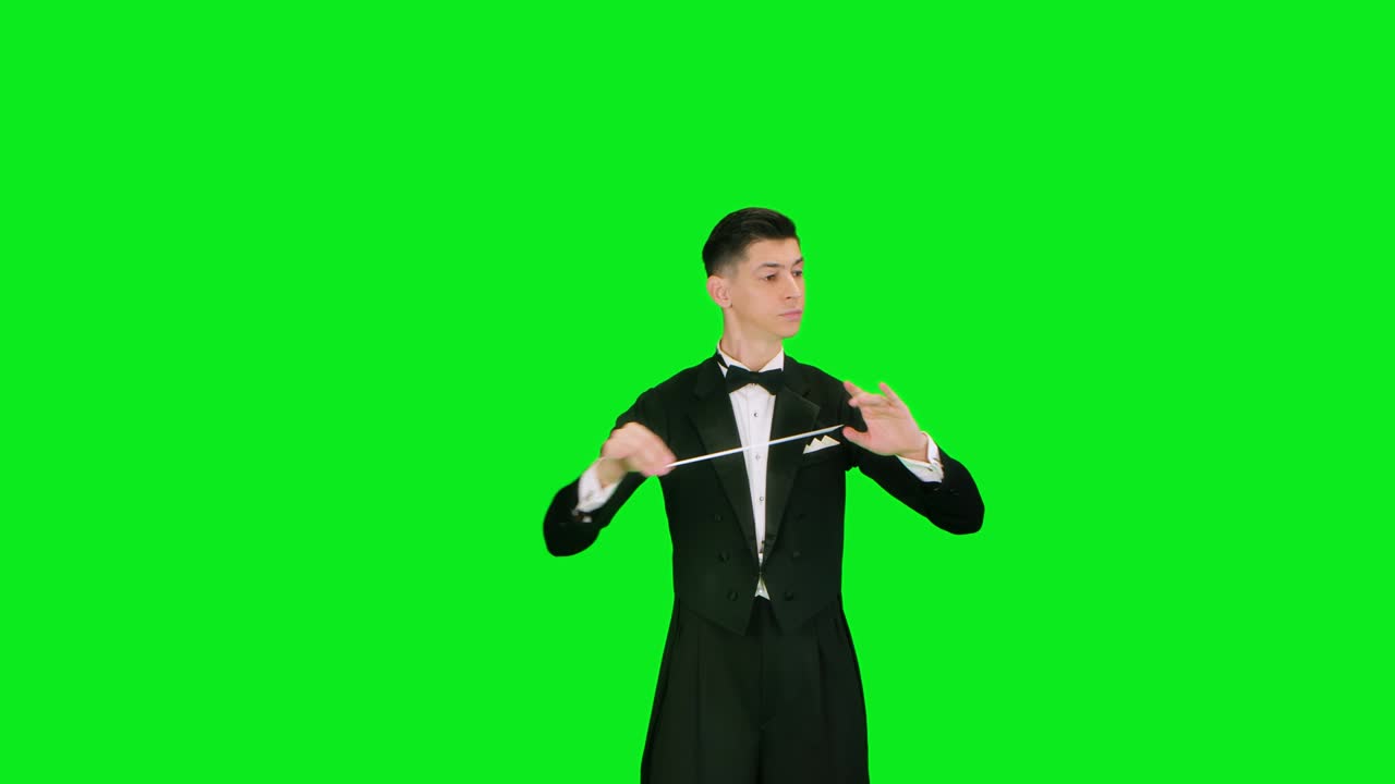 심포니 오케스트라의 지휘자는 슈트를 입고 음악가들을 지휘하고 있으며, 스튜디오에서 녹색 스크린에 고립되어 있으며, 가시적인 몸짓으로 음악 공연을 지휘하고 지휘하고 있습니다.