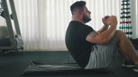 Toma-Lateral-De-Un-Joven-Fuerte-Haciendo-Abdominales-En-El-Gimnasio