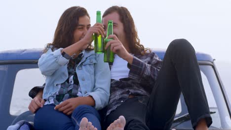 Couple-having-beer-while-sitting-on-car-bonnet-4k