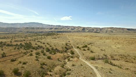 Eine-Einsame-Unbefestigte-Straße-Durchschneidet-Das-Grasland-Von-Arizona-Und-Verschwindet-In-Der-Ferne-In-Der-Bergkette