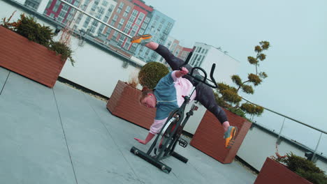 athletic girl performing aerobic training twine exercises on cycling stationary bike on house roof