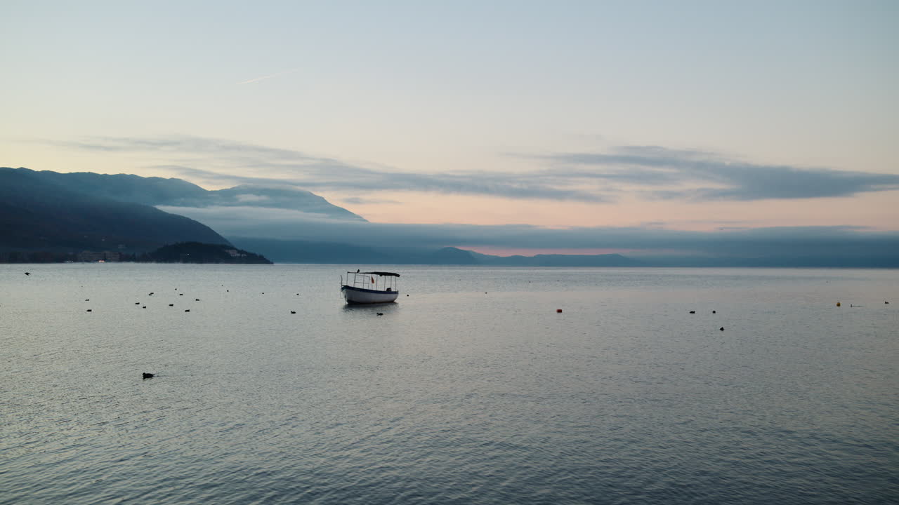 Barca da pesca che galleggia sulle calme acque del lago di Ocrida durante un'alba serena. Lago di Ocrida, Macedonia del Nord