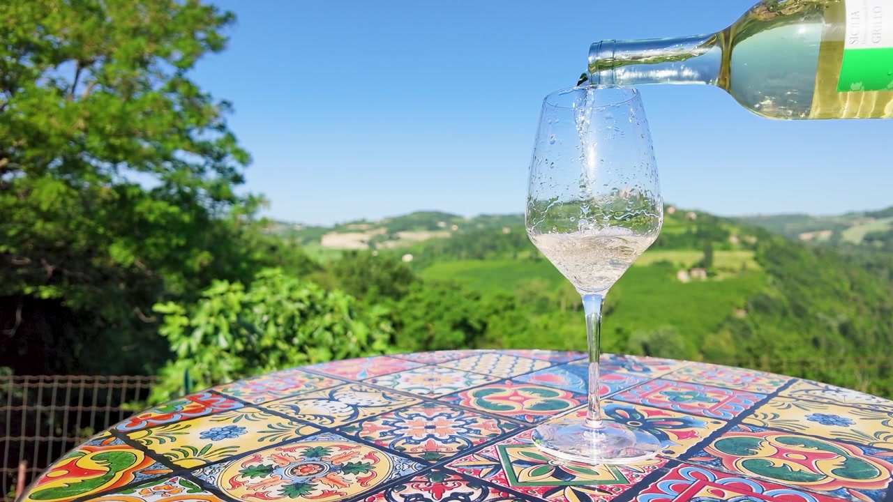Versare vino bianco in un bicchiere su un tavolo colorato con vista panoramica