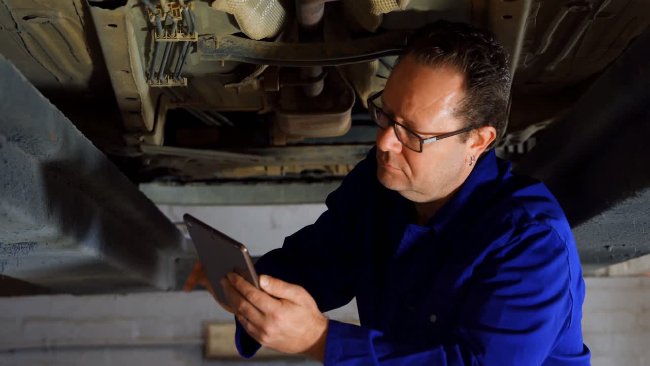 mecánico usando una tableta digital mientras examina un coche 4k
