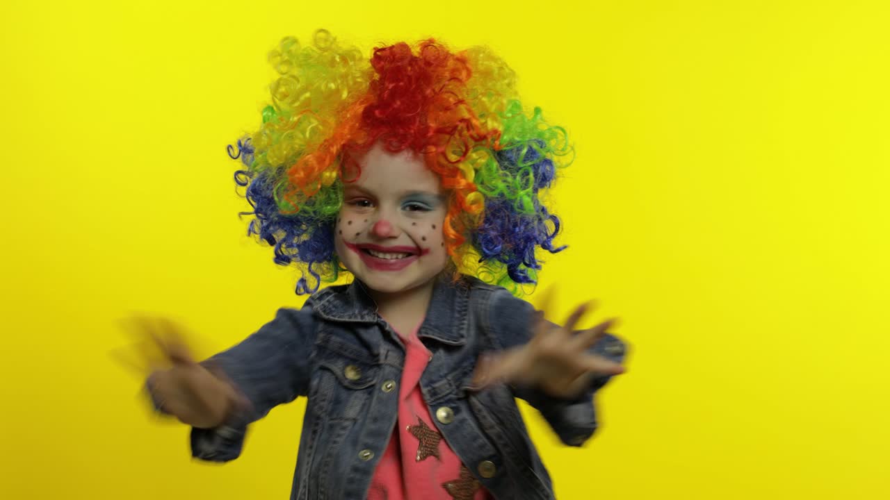 una niña payasa con una peluca colorida haciendo caras tontas. tonto, sonriendo, bailando. halloween