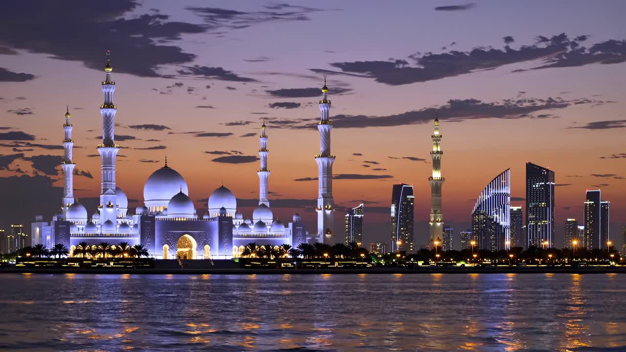 Scatto grandangolare di una grande moschea e di un moderno skyline al tramonto, che si riflettono sull'acqua