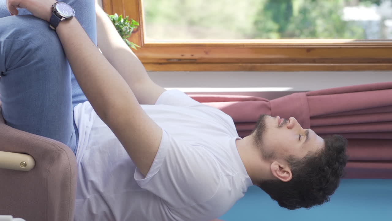 창문 앞에 있는 남자가 깊은 숨을 쉬고 눈을 감는 수직 영상입니다.