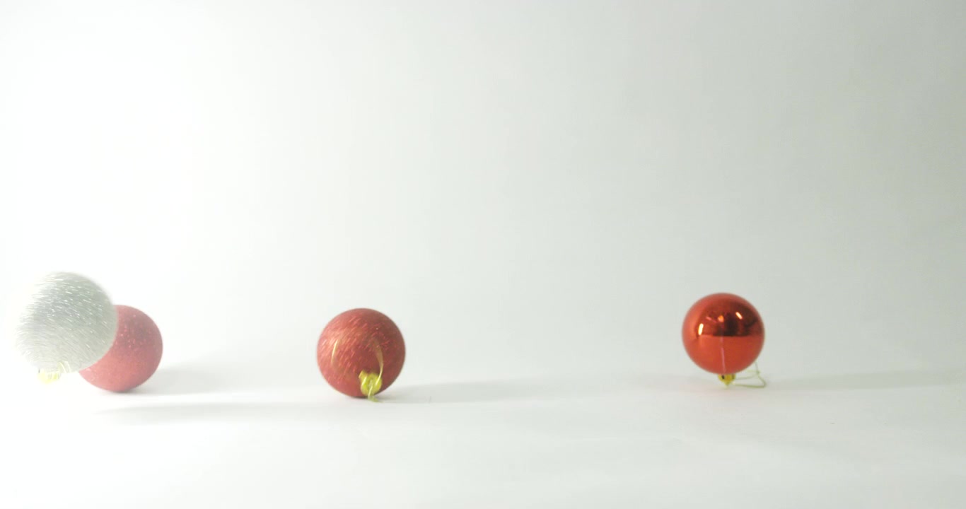 colourful Christmas bauble decorations falling from out of shot onto neutral light background.