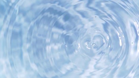 top view slow motion of drop falling into the water surface and diverging circles on white background