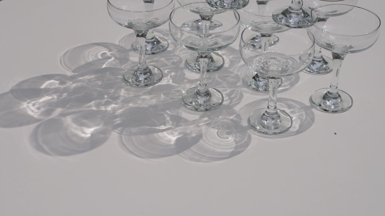 Tomme champagnecoupeglas arrangeret på et hvidt bord, der kaster bløde skygger til fejring