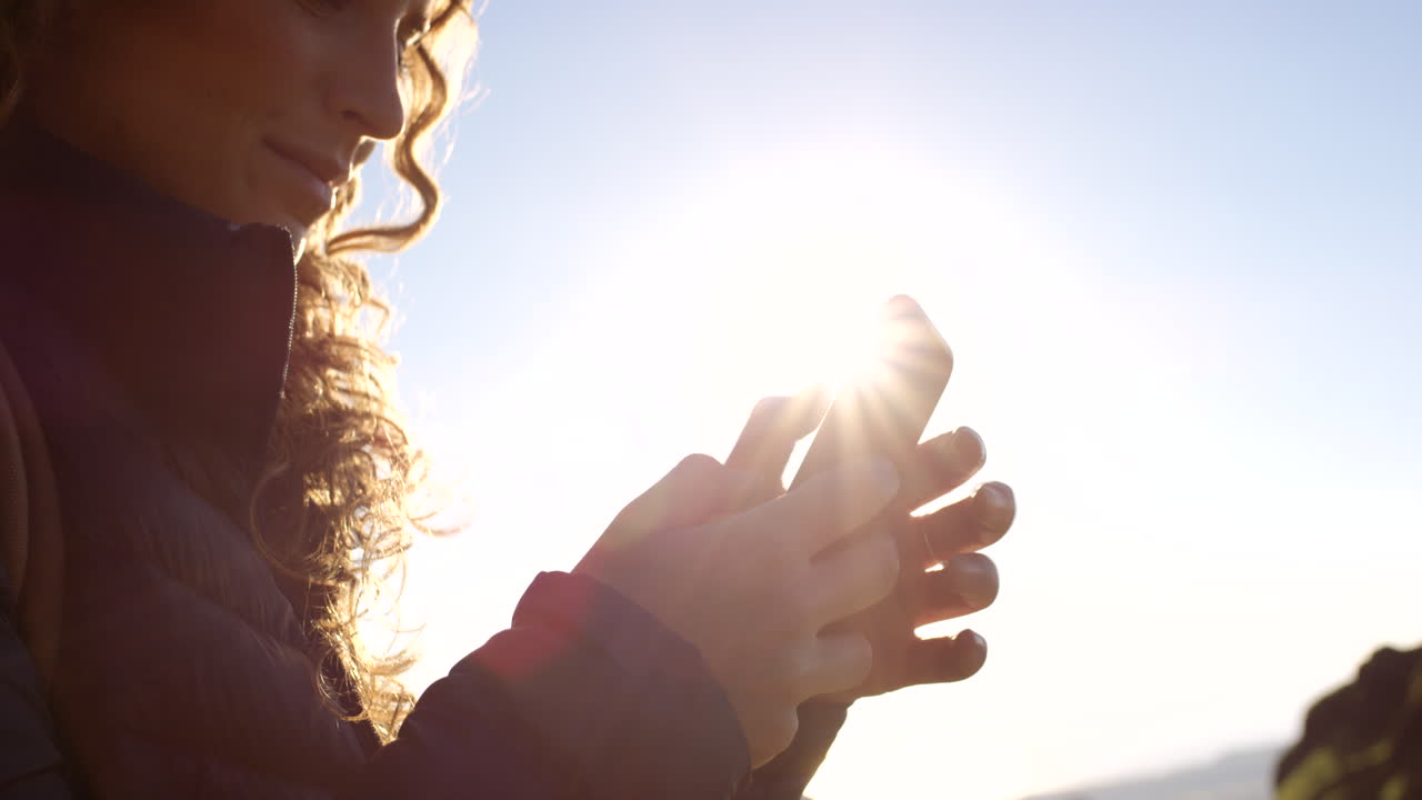 빛 아래 밖에서 스마트폰을 사용하는 여성