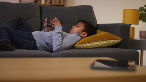 young boy lying on sofa at home playing game or streaming onto handheld gaming device 8