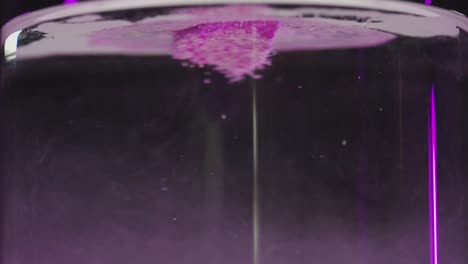 sal de baño rosa sostenida en agua con uñas moradas