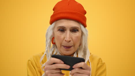 mujer de edad alegre celebrando en el interior. mujer emocionada jugando en el teléfono en el estudio.
