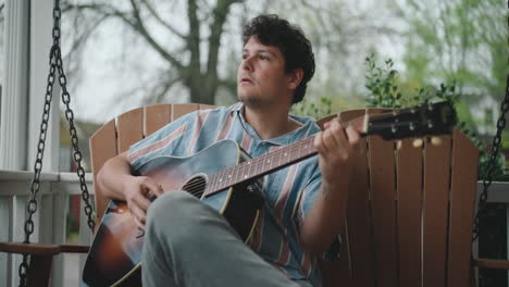 man playing acoustic guitar on a porch swing