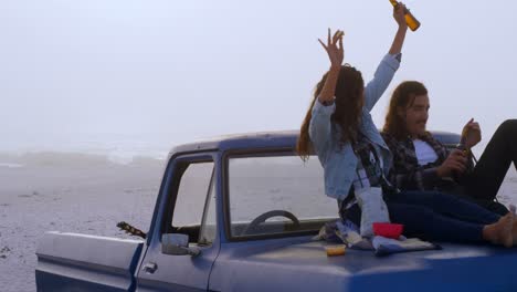 Couple-having-beer-while-sitting-on-car-bonnet-4k