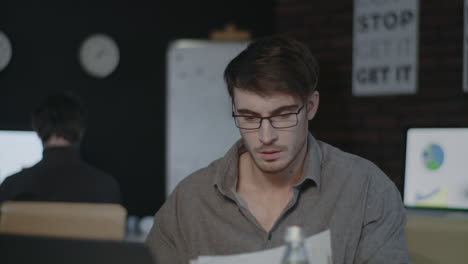 Concentrated-business-man-working-with-document-paper-near-laptop-in-dark-office