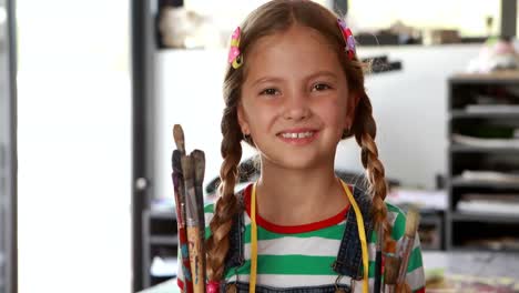 Portrait-of-cute-schoolgirl-standing-with-paintbrushes-4k