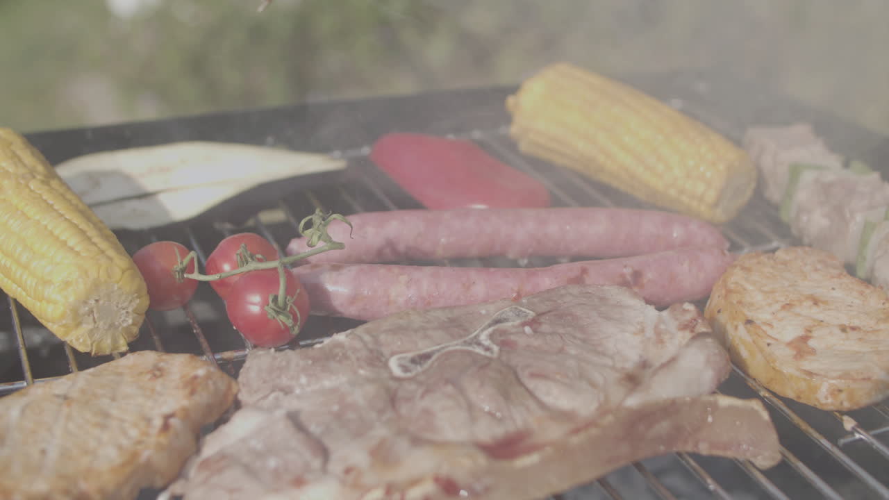 Close-up of tongs turning over pork and eggplant on grill