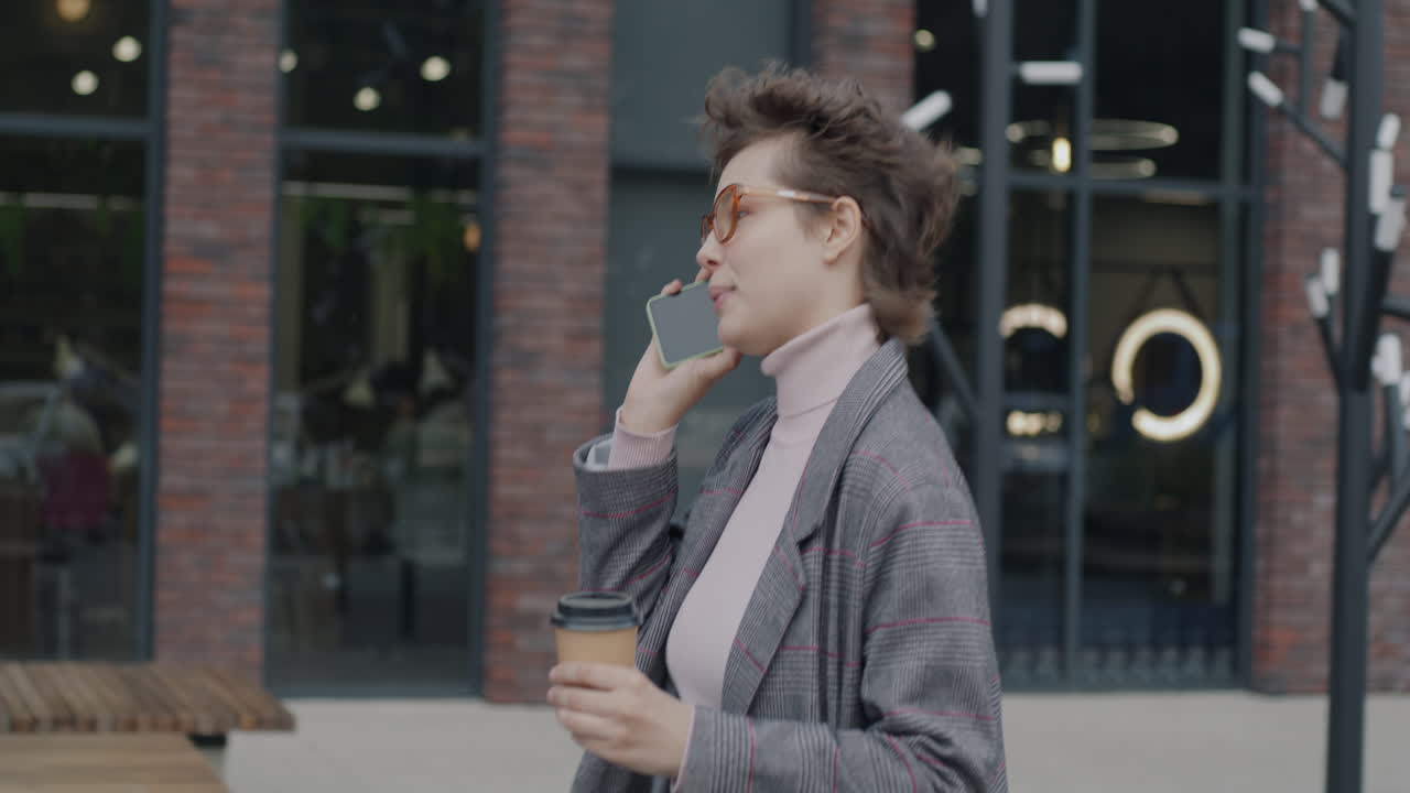 Young woman talking on phone while walking outside a modern building