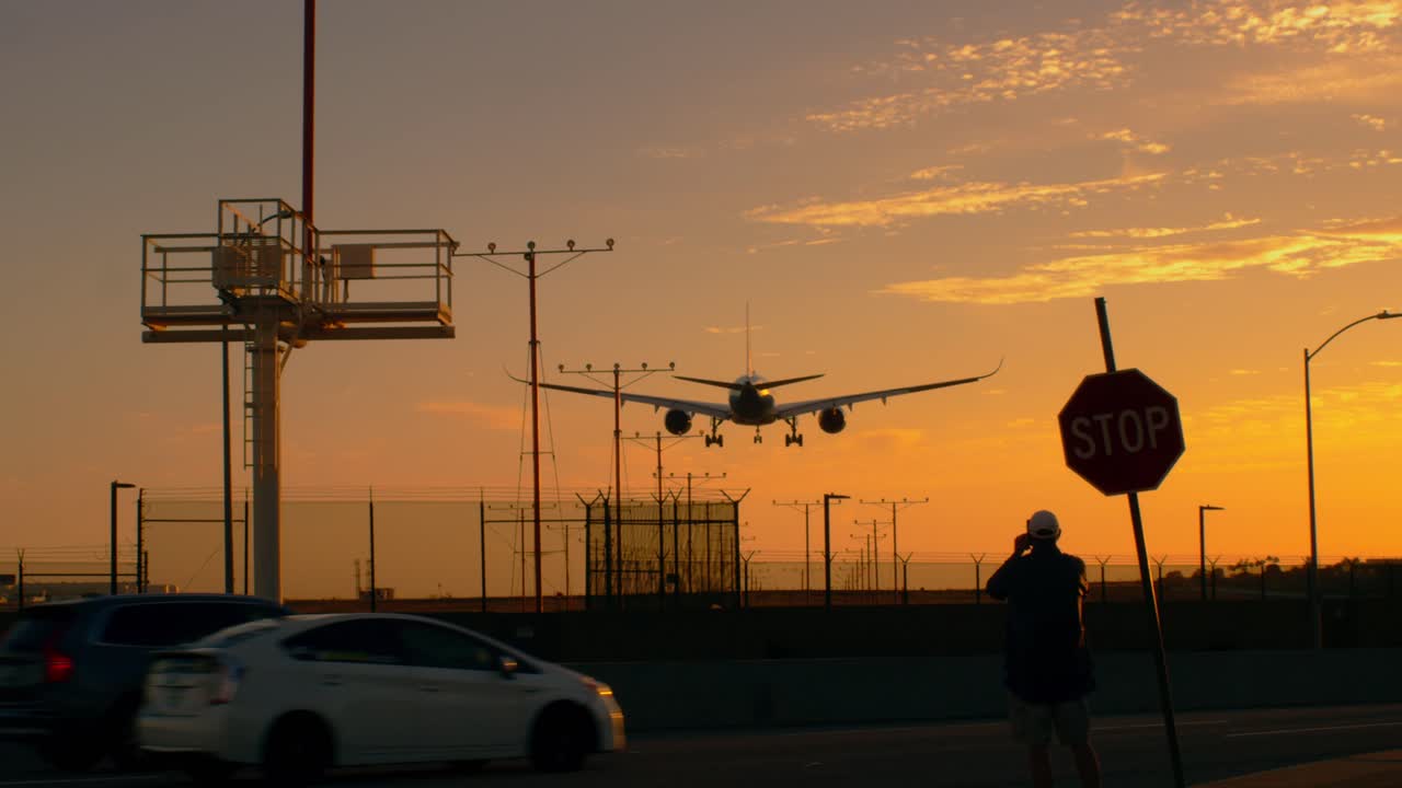 한 남자가 해가 지면 락스 로스앤젤레스에 착륙하는 2엔진 실루 ⁇  여객기를 촬영하고 있다.