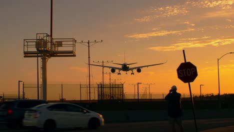 Hombre-Filmando-Un-Avión-De-Pasajeros-Con-Silueta-Bimotor-Aterrizando-En-Lax-Los-Ángeles-Al-Atardecer