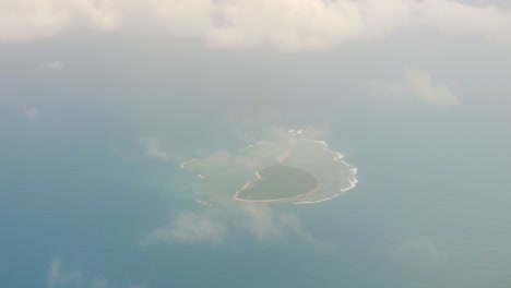 bird's-eye perspective from airplane window with view of uninhabited tropical island and small clouds