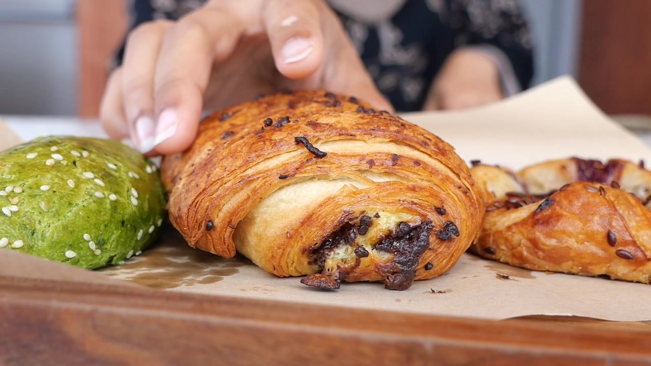 Persona che prende un cornetto al cioccolato fresco da un vassoio di pasticceria