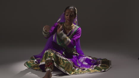 primer plano de una bailarina de kathak femenina realizando un baile vestida con un vestido tradicional indio sentada en el suelo en el centro de atención 4