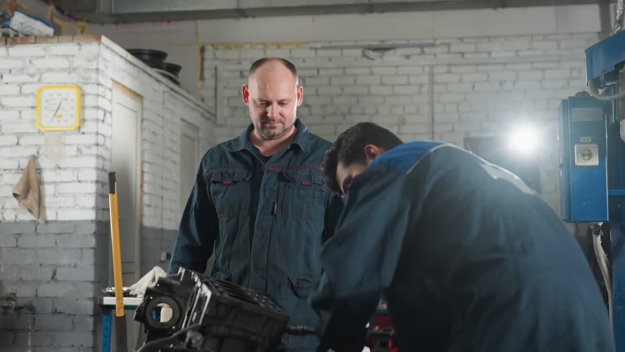 profesionales en el taller mecánico trabajando en el motor del coche, apretando la tuerca con guantes rojos mientras el colega observa, el fondo presenta herramientas de trabajo, reloj de pared amarillo y luz brillante