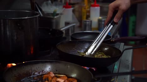 slow motion close up shot capturing chef cooking spaghetti aglio olio pasta with bacon, flipping, mixing and stirring the ingredients in the frying pan on stovetop