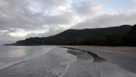 aerial view low and fast over the barra do sahy beach, cloudy sunset in brazil