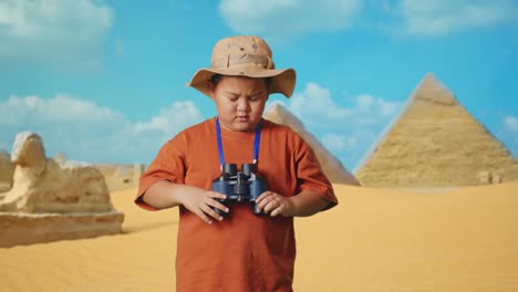 asian boy with a hat having a headache after looking through the binoculars. boy researcher examines something while traveling in giza pyramid, travel tourism adventure concept