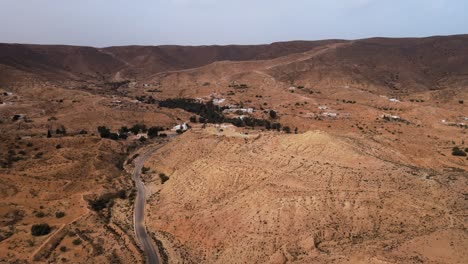 aerial view of a winding road through a desert landscape in ksar hallouf, tunisia, with scattered houses and vegetation.