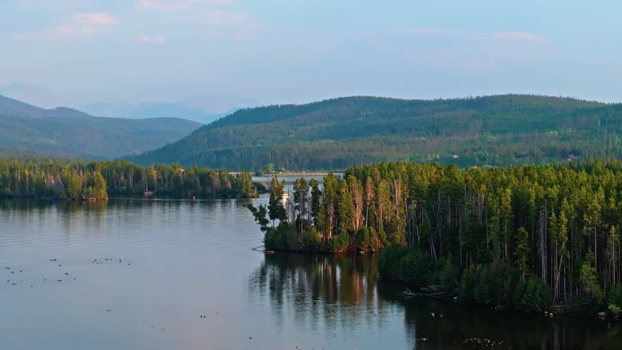Drone ascend reveal above still Grand Lake Colorado showing mirror reflections of forested mountains in calm water light