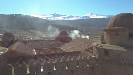 Absteigende-Luftaufnahme-über-Der-Burg-Von-La-Calahorra-Mit-Sierra-Nevada-Dahinter-An-Einem-Sonnigen-Wintertag