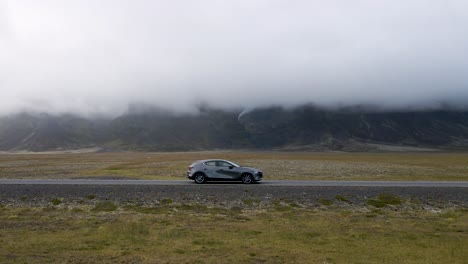 A-grey-2021-Mazda-3-advances-along-an-Icelandic-road,-the-journey-highlighted-by-open-grassy-plains-and-a-cloudy-sky,-encapsulated-in-smooth-4K