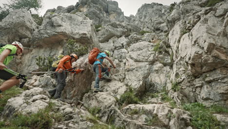 hikers wearing backpacks and helmets climbing up a steep part of a climb on a mountain