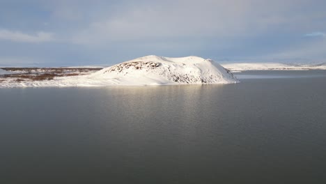 isolated snowy mountain surrounded by water in the north of iceland at sunset, aerial