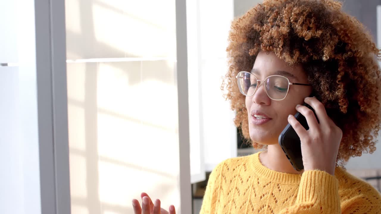 Empresária casual birracial feliz falando no smartphone em escritório ensolarado, câmera lenta.