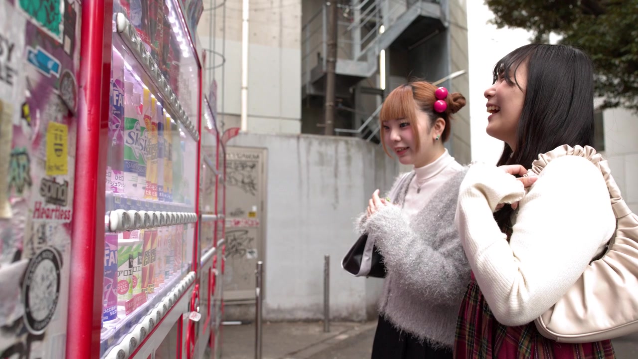 Due amici con abiti invernali alla moda guardano un distributore automatico per strada a Tokyo, Giappone