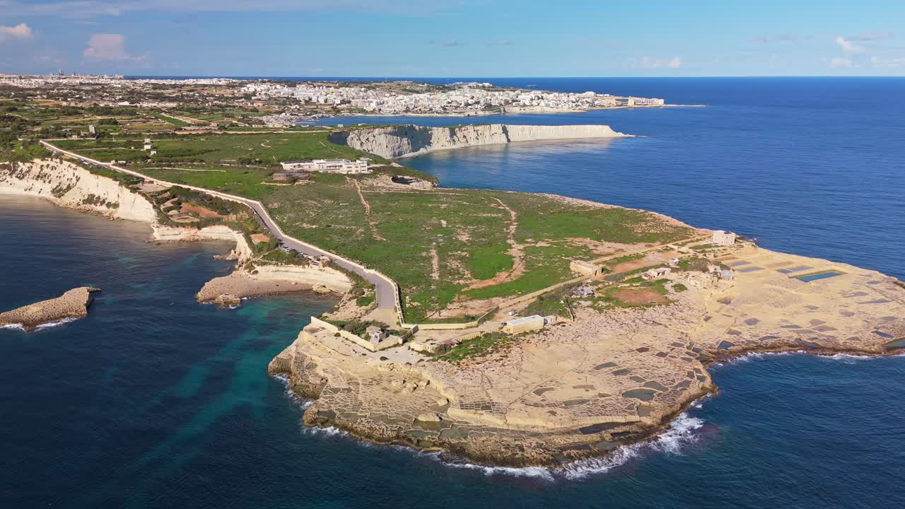 Dronebilde i bane over Triq Xrobb L-Għaġin på sørlige Malta, som viser en robust halvøy, saltpanner og et feiende middelhavslandskap med Marsaskala i det fjerne på en solrik vinterdag