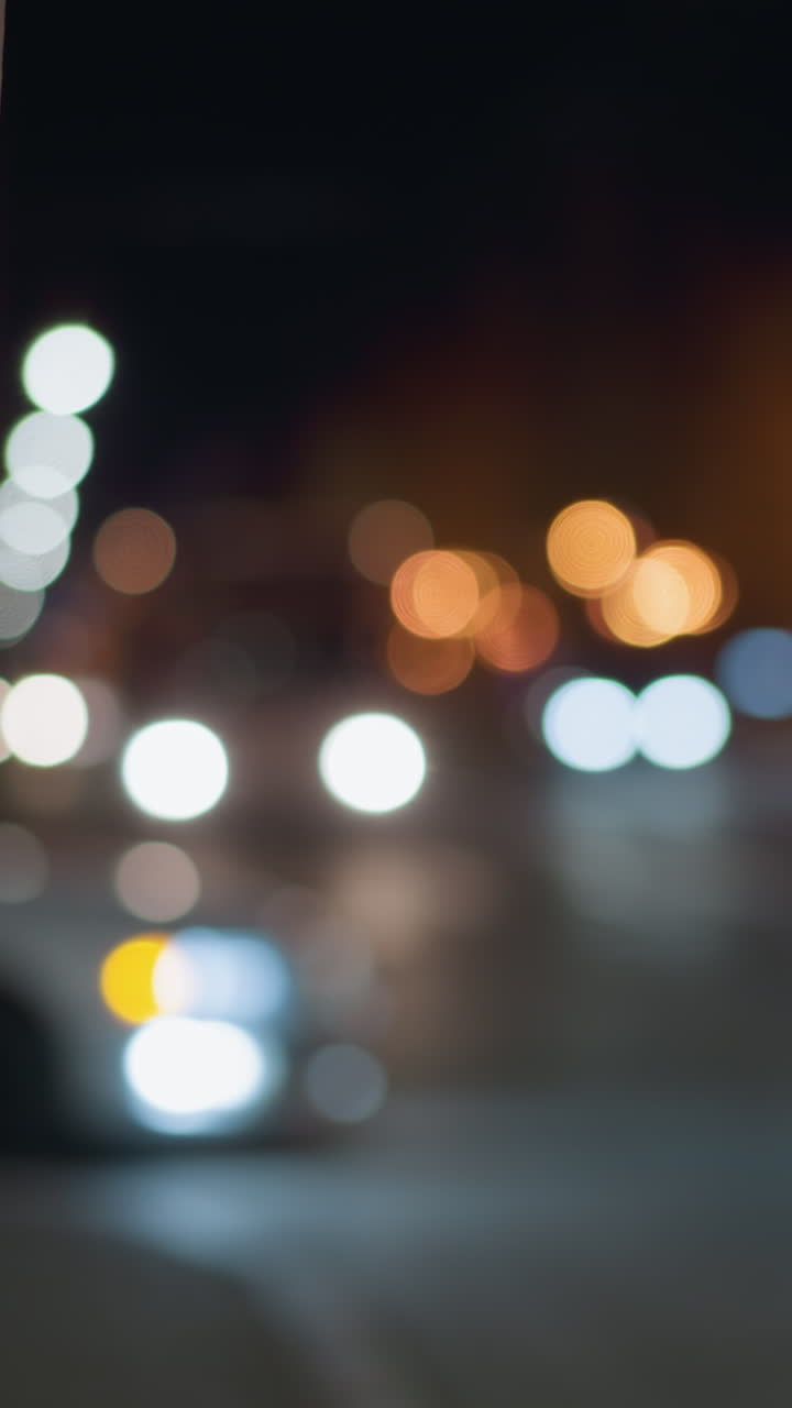 vista bokeh de una escena nocturna de la ciudad con coches borrosos y luces de la calle en el fondo, capturada con un enfoque en un poste de la calle cercana