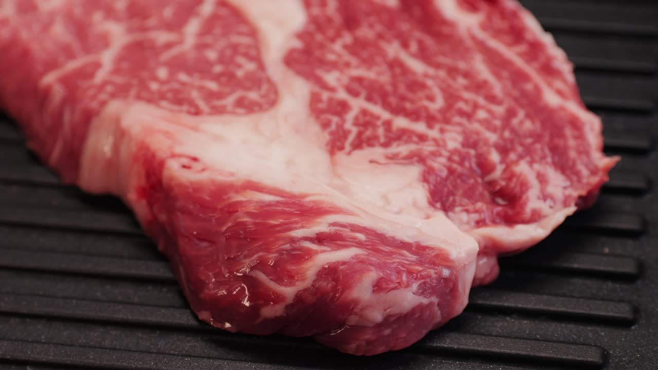 Manzo fresco marmorizzato con pepe, sale e rosmarino, primo piano macro. Preparazione per cucinare una succulenta bistecca alla griglia. Carne wagyu cruda biologica premium. Filmato 4K di alta qualità.