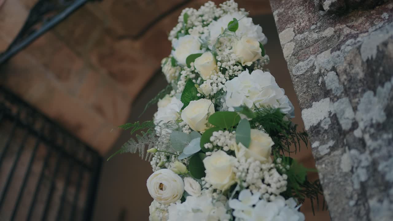 Close up of fresh white roses and greenery arranged on a rustic stone arch for wedding decor