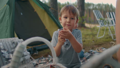 un niño en edad preescolar está jugando con un cuchillo plegable en un picnic familiar en un campamento de tiendas de campaña en el bosque para la familia