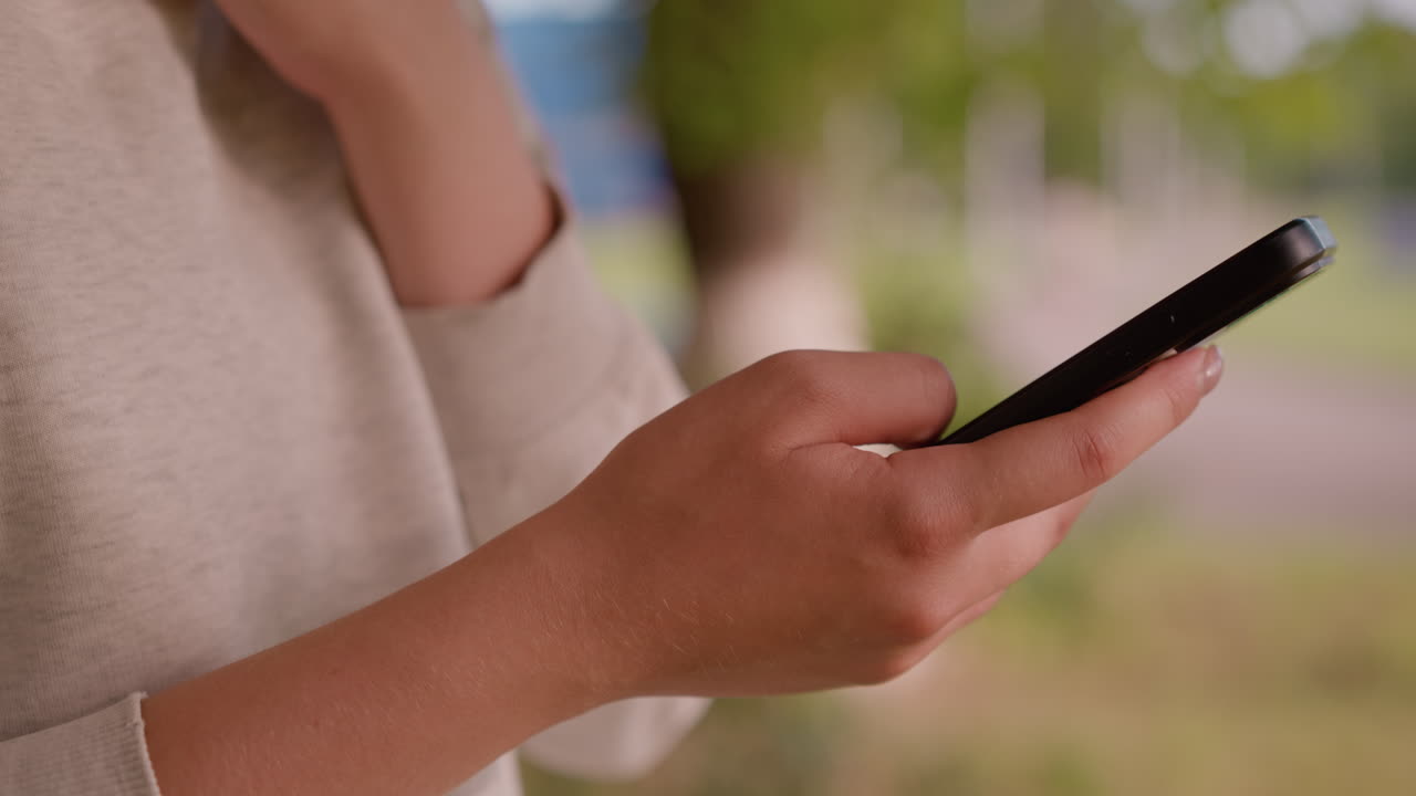 primer plano de un teléfono inteligente individual que opera a mano con enfoque en las manos, fondo natural borroso con vegetación y figura poco clara en la distancia