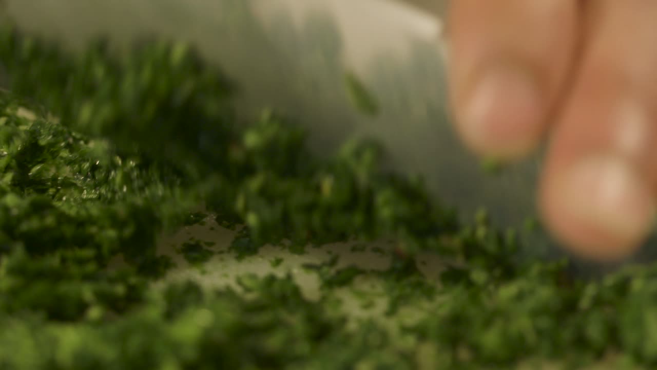 primer plano de los dedos cortando hierbas verdes frescas en una tabla de cortar