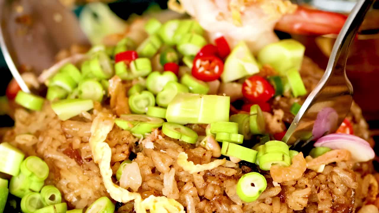 Close-up of vibrant vegetables being added to fried rice, highlighting fresh ingredients and colorful presentation.